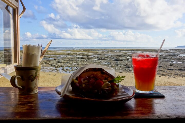 Red iced drink and a sandwich on a counter by an open window onto the sea