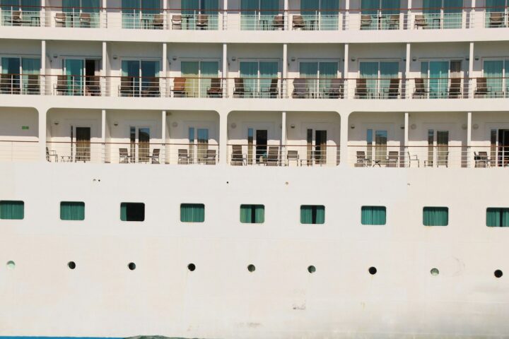 Side of a cruise ship showing balcony decks above rows of portholes