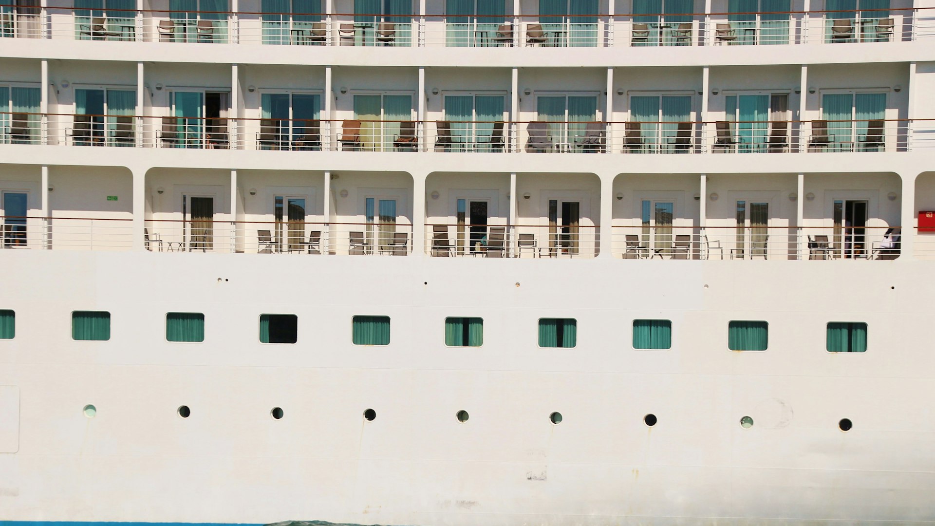 Side of a cruise ship showing balcony decks above rows of portholes