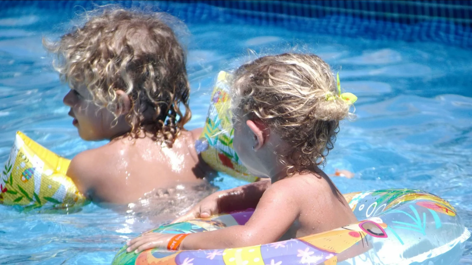 Two small children playing in a pool with floats