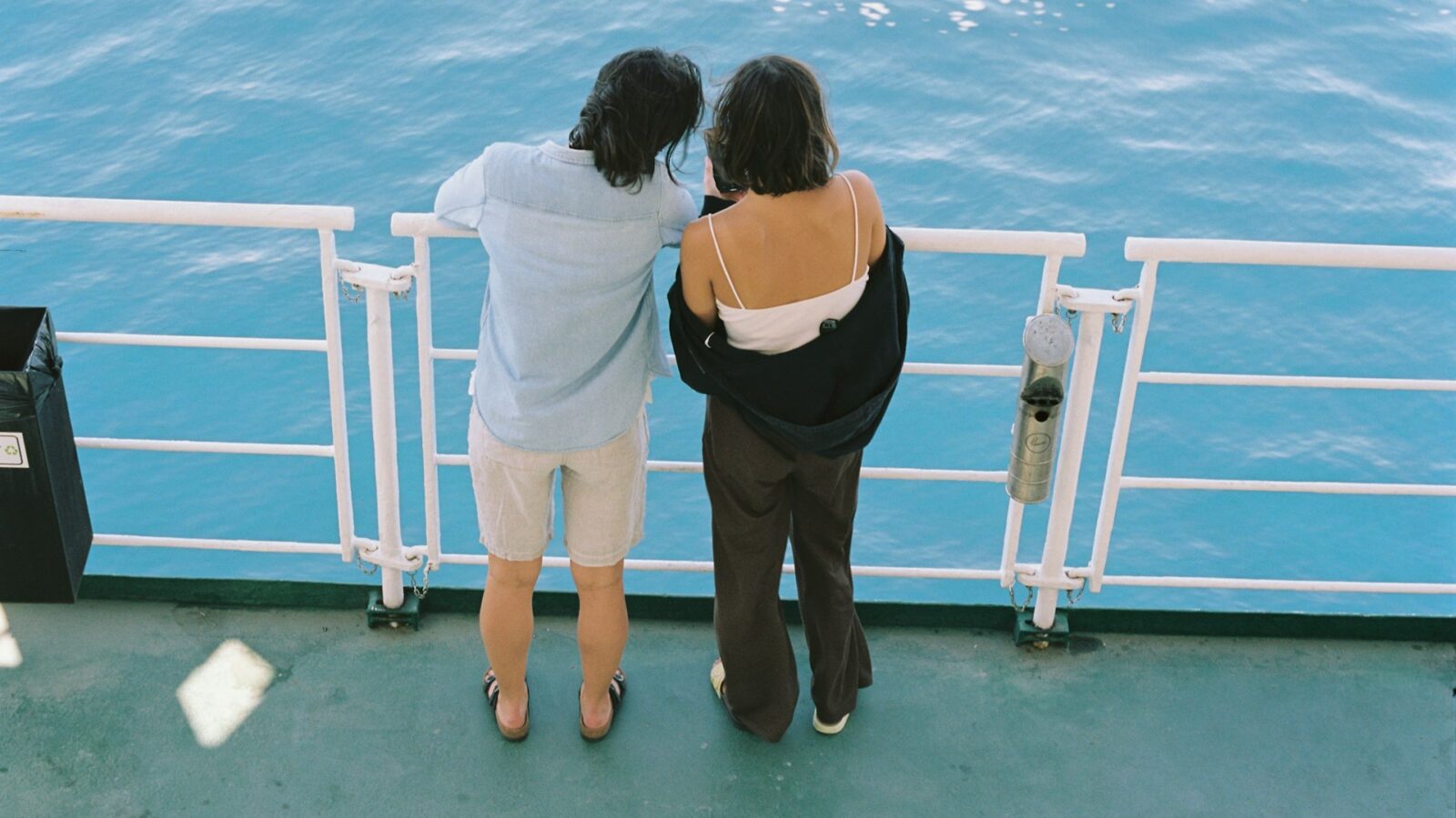 Two friends leaning on a ship railing above bright blue sea