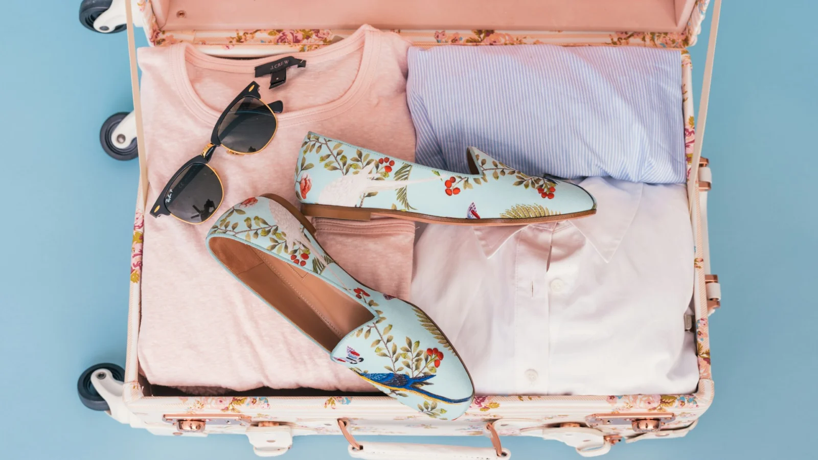 Open pink suitcase with sunglasses and loafers packed on top