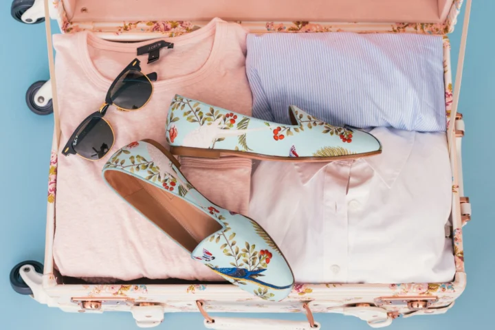 Open pink suitcase with sunglasses and loafers packed on top